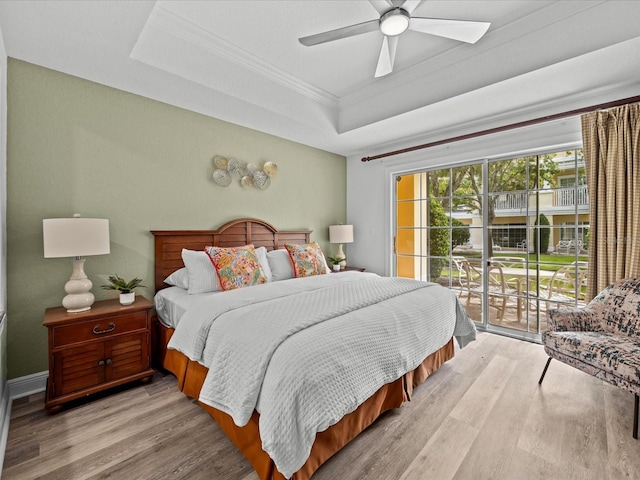 bedroom with ornamental molding, light wood-style floors, a raised ceiling, and access to exterior