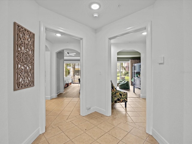 corridor with a wealth of natural light, arched walkways, and light tile patterned floors