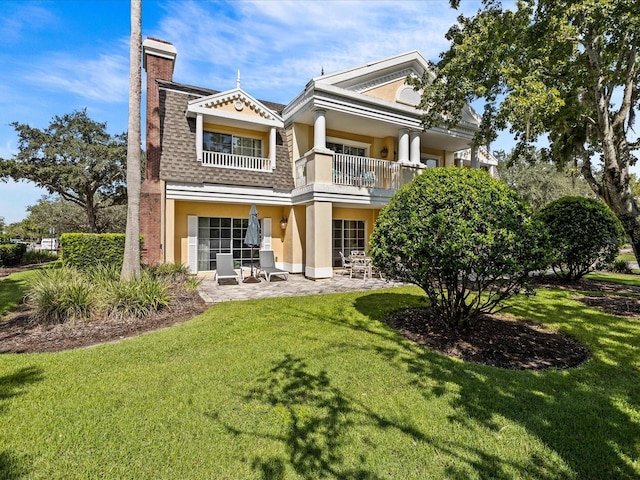 back of house with a patio, a chimney, a shingled roof, a lawn, and a balcony