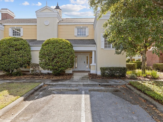 view of front of house featuring a shingled roof, uncovered parking, and stucco siding