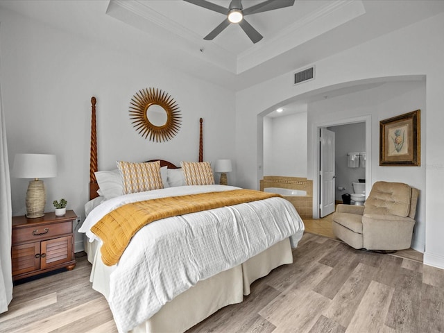 bedroom with ceiling fan, light hardwood / wood-style floors, a raised ceiling, and ensuite bath