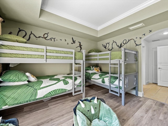 bedroom featuring wood-type flooring, a raised ceiling, and ornamental molding