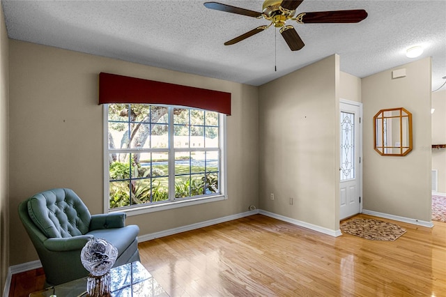 living area featuring ceiling fan, light wood-type flooring, and a textured ceiling