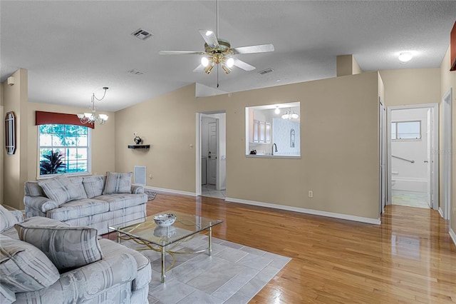 living room featuring ceiling fan with notable chandelier, light hardwood / wood-style flooring, and a textured ceiling