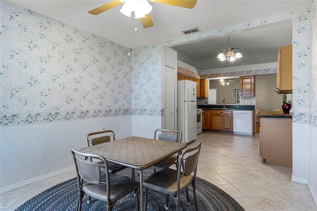 dining space featuring light tile patterned floors, ceiling fan with notable chandelier, sink, and a textured ceiling