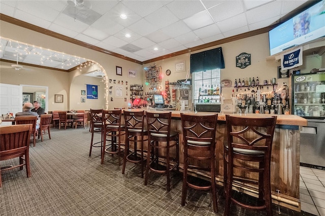 bar with carpet floors, ceiling fan, a paneled ceiling, and crown molding