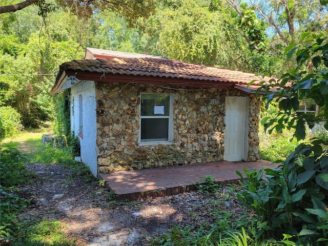 view of property exterior featuring a tile roof, stone siding, and an outdoor structure