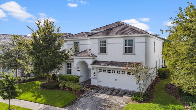 mediterranean / spanish house featuring a garage, decorative driveway, a tile roof, and a front lawn