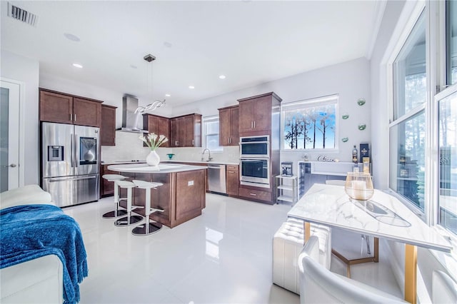 kitchen featuring hanging light fixtures, backsplash, stainless steel appliances, wall chimney range hood, and a kitchen island