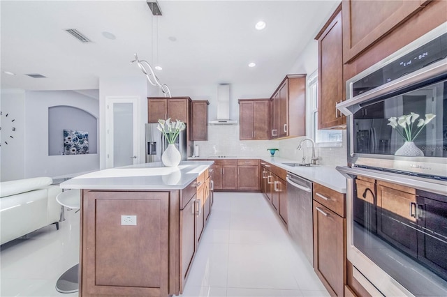 kitchen with decorative light fixtures, stainless steel appliances, a kitchen island, sink, and wall chimney range hood