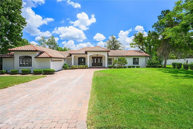 mediterranean / spanish-style house featuring decorative driveway, a tile roof, stucco siding, a front yard, and a garage