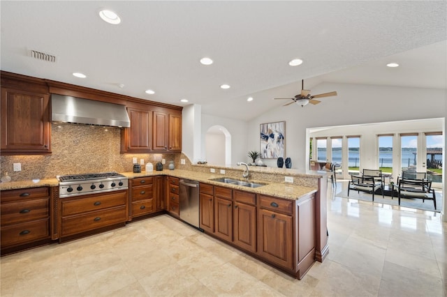 kitchen with stainless steel appliances, light stone counters, sink, ceiling fan, and wall chimney exhaust hood