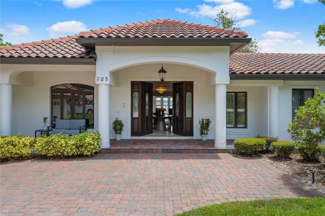 view of exterior entry featuring covered porch, a tile roof, and stucco siding