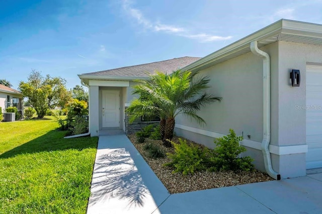 view of exterior entry featuring an attached garage, stucco siding, cooling unit, and a yard