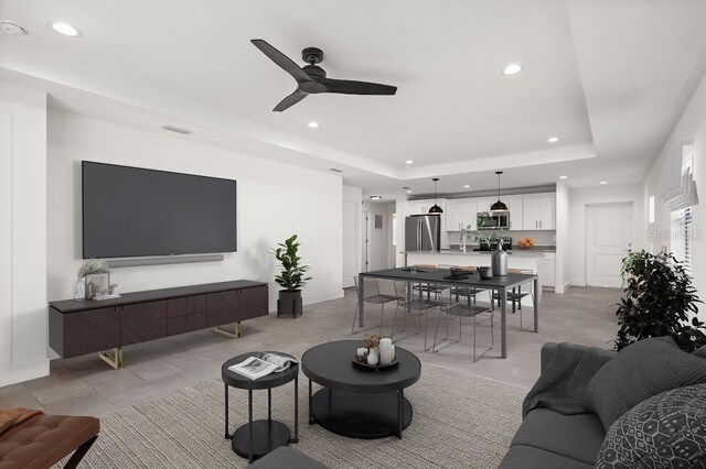 tiled living room with ceiling fan and a tray ceiling