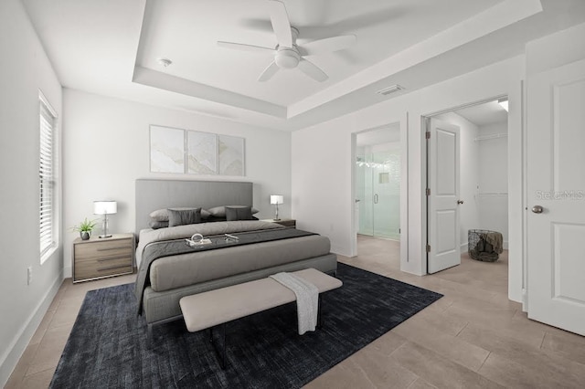 bedroom with ceiling fan, ensuite bathroom, and a tray ceiling