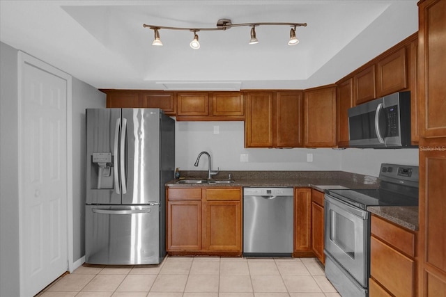 kitchen with stainless steel appliances, brown cabinets, a sink, and light tile patterned floors