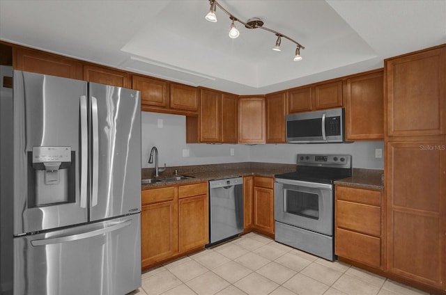 kitchen featuring appliances with stainless steel finishes, a tray ceiling, brown cabinetry, and a sink