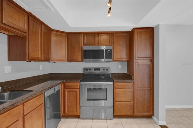 kitchen featuring dark stone counters, track lighting, appliances with stainless steel finishes, and light tile patterned floors