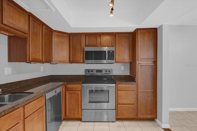 kitchen featuring light tile patterned floors, appliances with stainless steel finishes, brown cabinets, dark stone counters, and a raised ceiling