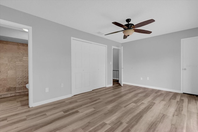 unfurnished bedroom with baseboards, ensuite bath, ceiling fan, wood finished floors, and a closet