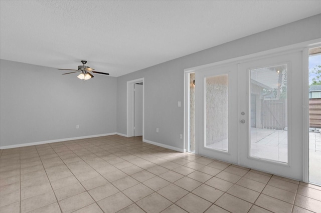 empty room featuring french doors, a ceiling fan, light tile patterned flooring, a textured ceiling, and baseboards