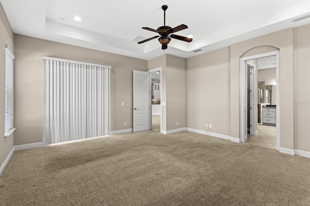 unfurnished bedroom with a raised ceiling, ceiling fan, light carpet, and connected bathroom