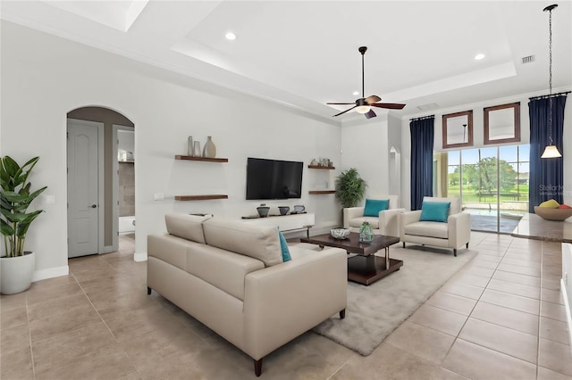 living room with ceiling fan, a tray ceiling, and crown molding