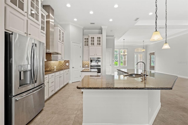 kitchen featuring stainless steel appliances, wall chimney range hood, sink, and a spacious island