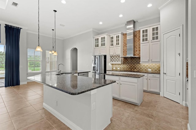 kitchen featuring sink, a kitchen island with sink, wall chimney exhaust hood, and stainless steel refrigerator with ice dispenser