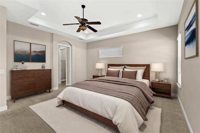 bedroom with ceiling fan, light carpet, and a tray ceiling