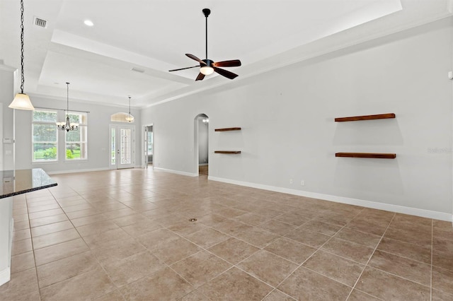 unfurnished living room with ceiling fan with notable chandelier, ornamental molding, a tray ceiling, and light tile patterned floors