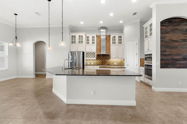 kitchen with wall chimney exhaust hood, decorative light fixtures, stainless steel appliances, a large island, and dark stone counters