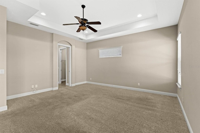 carpeted empty room with ceiling fan, a tray ceiling, and a healthy amount of sunlight