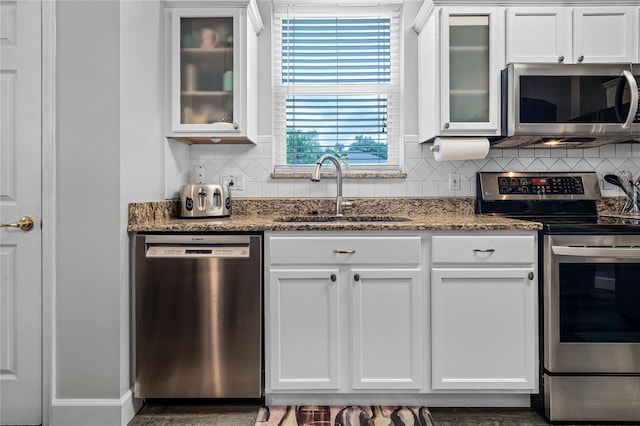 kitchen with appliances with stainless steel finishes, white cabinetry, sink, and backsplash