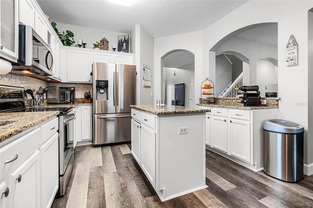 kitchen featuring appliances with stainless steel finishes, wood-type flooring, tasteful backsplash, and a kitchen island