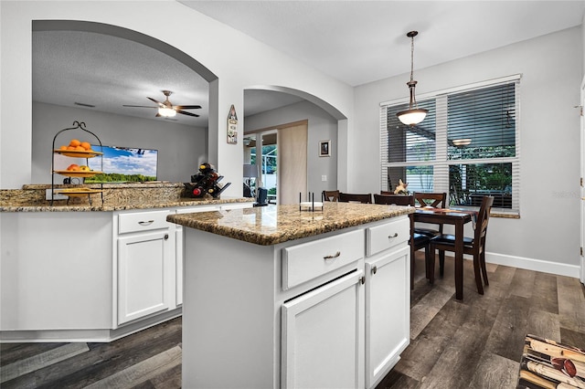 kitchen with decorative light fixtures, white cabinetry, stone countertops, a center island, and dark wood-type flooring