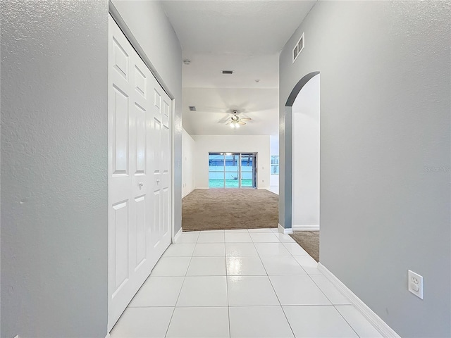 hall featuring carpet floors, arched walkways, visible vents, tile patterned flooring, and baseboards