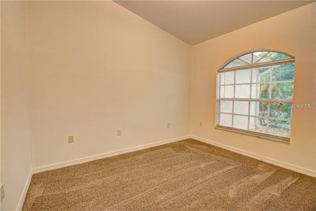 empty room with carpet, vaulted ceiling, and baseboards