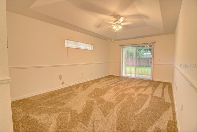 empty room featuring carpet floors, ceiling fan, a tray ceiling, and baseboards