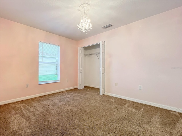 unfurnished bedroom with a notable chandelier, a closet, visible vents, carpet flooring, and baseboards