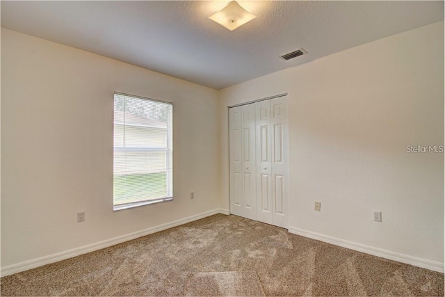 unfurnished bedroom with a textured ceiling, carpet flooring, visible vents, baseboards, and a closet