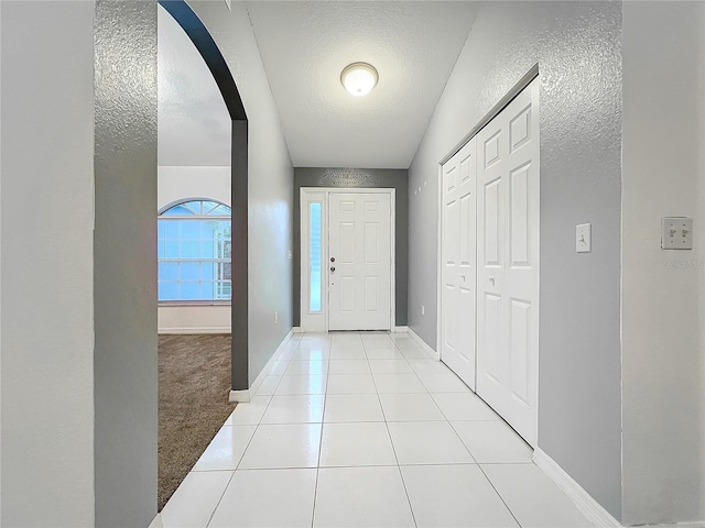 entrance foyer featuring arched walkways, light tile patterned floors, light colored carpet, a textured ceiling, and baseboards