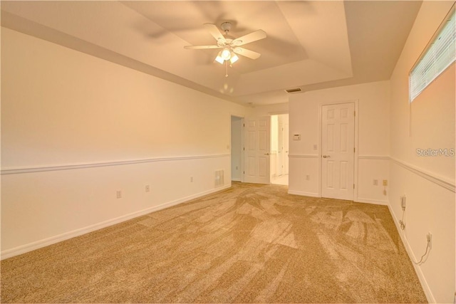 spare room featuring light carpet, baseboards, visible vents, and a raised ceiling