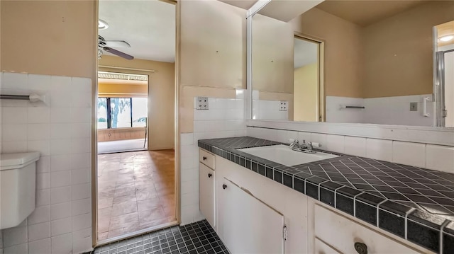 bathroom with ceiling fan, toilet, vanity, tile walls, and tile patterned floors