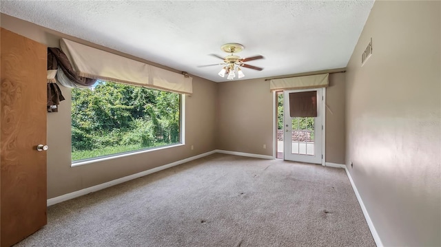 carpeted empty room featuring a textured ceiling, plenty of natural light, and visible vents