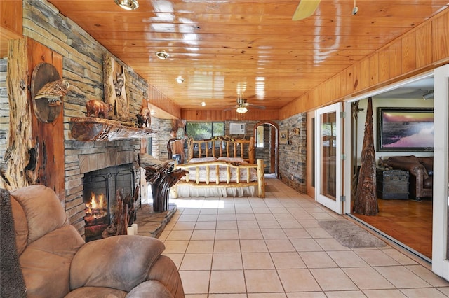 unfurnished living room with a ceiling fan, wood ceiling, light tile patterned flooring, and a stone fireplace