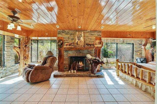 tiled living area featuring wooden ceiling, a ceiling fan, and a stone fireplace