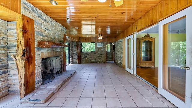 unfurnished living room with a ceiling fan, wooden ceiling, an outdoor stone fireplace, and light tile patterned floors