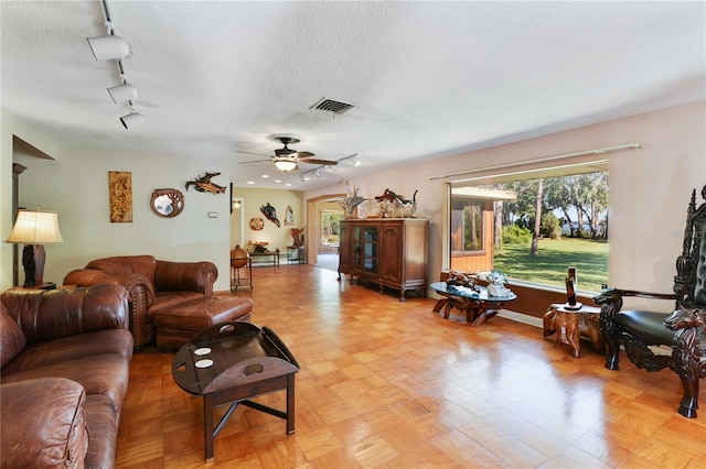 living room with visible vents, baseboards, ceiling fan, rail lighting, and a textured ceiling